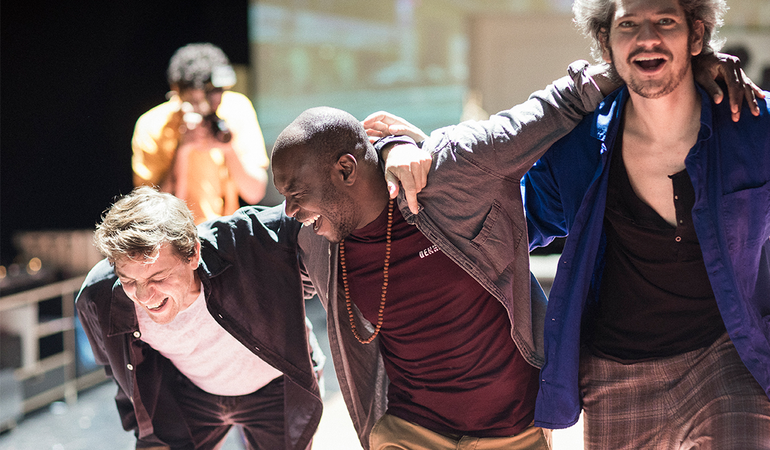Three men are laughing with their arms around each others shoulders. They are wearing t-shirts and jackets