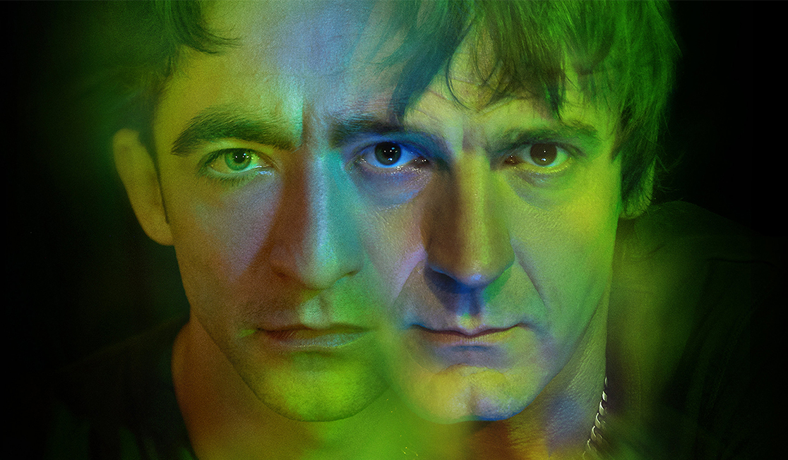 Two faces are shown in a green light with a dark background, both people have short brown hair. Their faces are slightly merged together.
