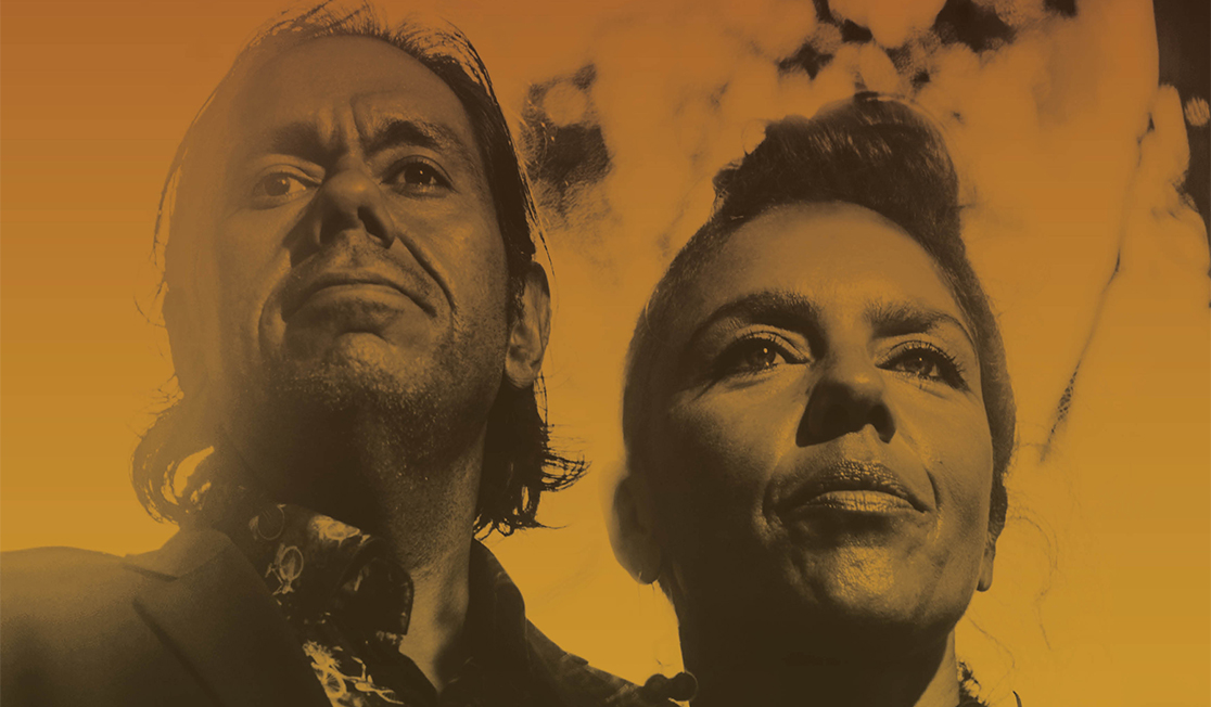 A low angle shows two people's faces. The image is filtered orange and the man and woman both have dark hair and are smiling. 