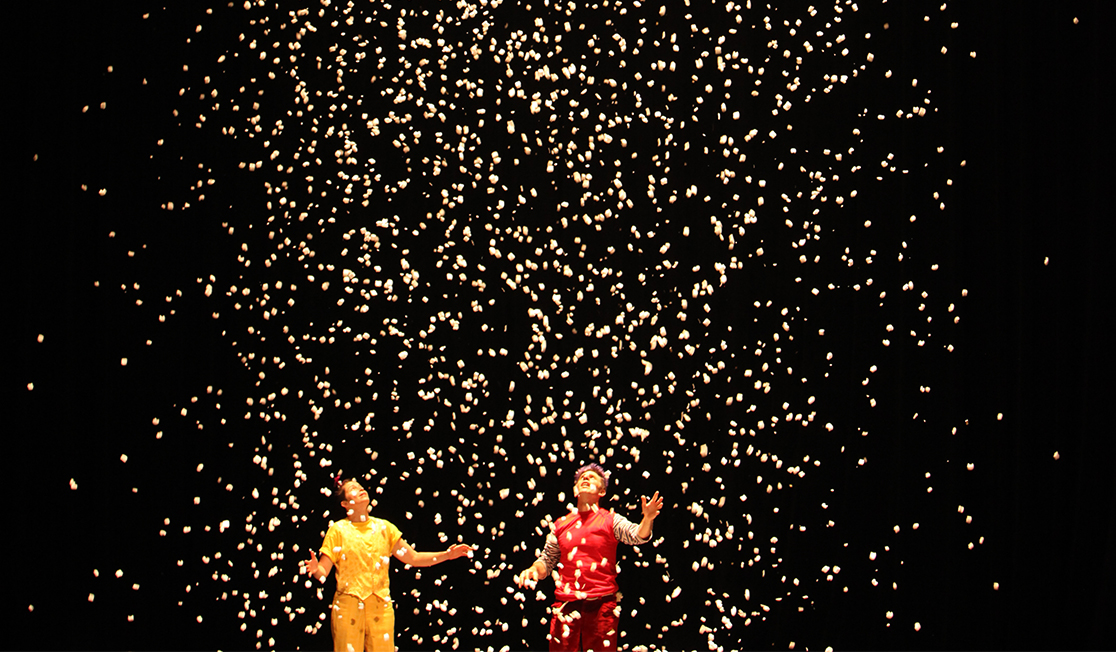 Two people look up into the air as fake snow falls around them.