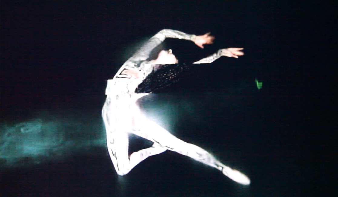 A person wearing white and shown in bright light is leaping with their arms and head leaned back, They are pictured on a black background.